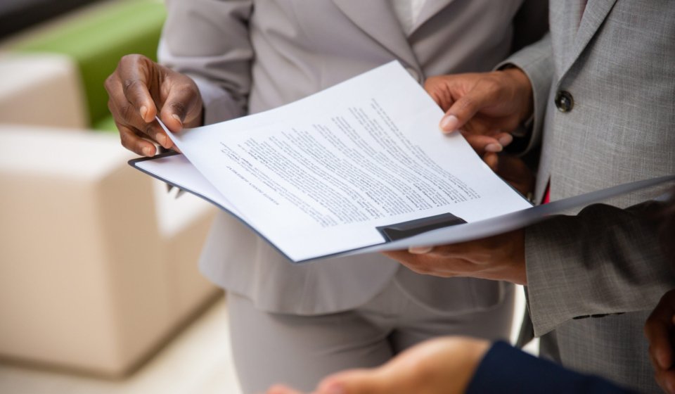 Diverse business partners reading contract together. Business man and woman wearing formal suits, standing and holding open folder with document. Agreement concept